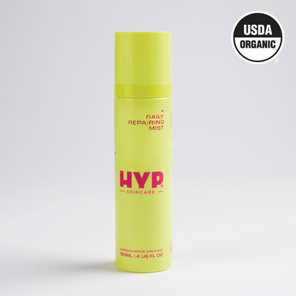 A standalone image of a bright yellow bottle of 'HYP Daily Repairing Mist' set against a plain white background. The product is labeled with the brand name 'HYP' in large pink letters and the words 'Daily Repairing Mist' above it. The 'USDA ORGANIC' seal is visible in the upper right corner of the bottle, certifying its organic status.