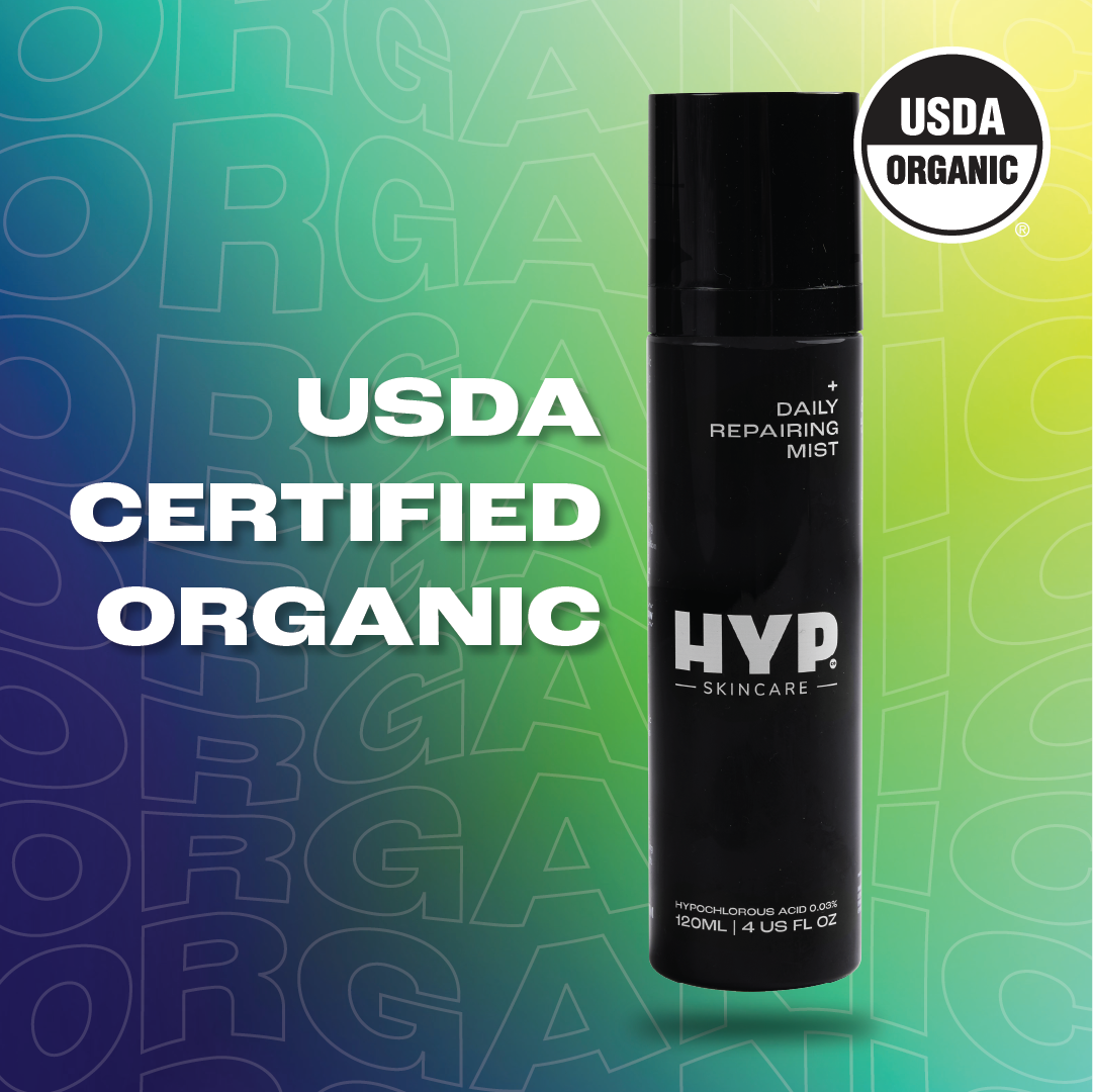 Image showcasing a black bottle of 'HYP Daily Repairing Mist' skincare product against a gradient blue and green background patterned with multiple 'ORGANIC' texts. Prominent text overlay in white reads 'USDA CERTIFIED ORGANIC,' aligning with the 'USDA ORGANIC' seal displayed on both the upper right corner of the image and the bottle itself, highlighting the product's organic certification status.